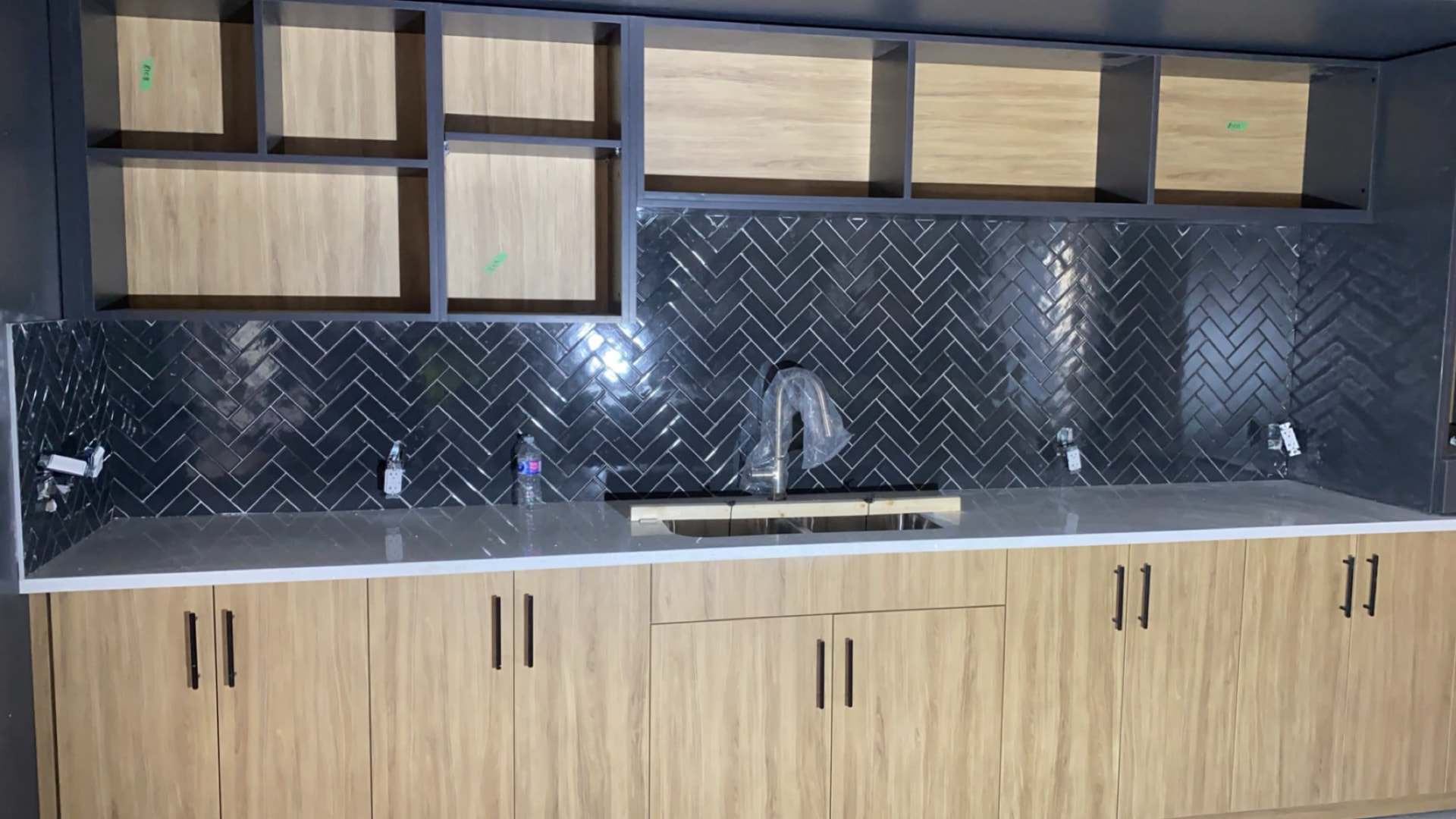 Kitchen cabinetry with a dark patterned tile backsplash